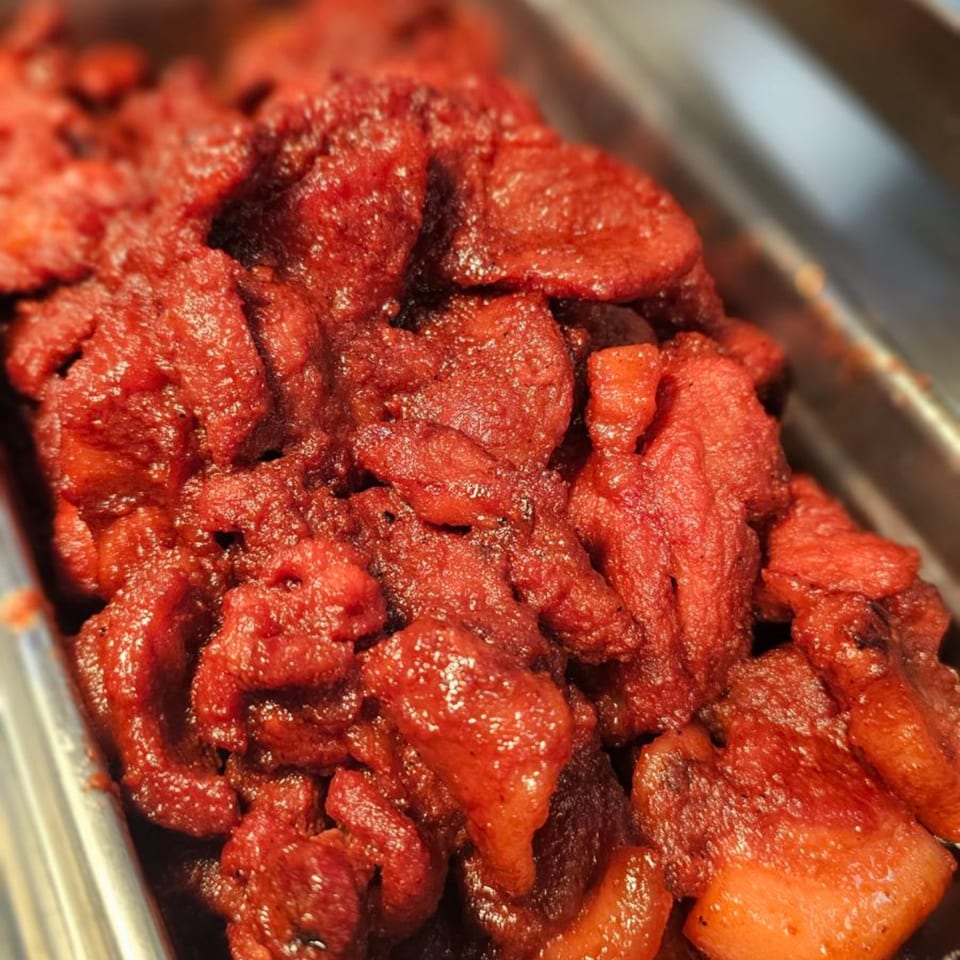Close-up of Kujo Eats' bright red, glistening Filipino pork tocino in a metal serving tray.