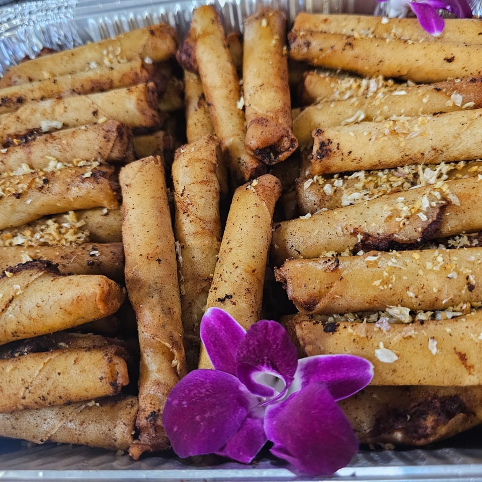 A close-up of Kujo Eats' Filipino lumpia, golden-brown and garnished with a purple orchid.