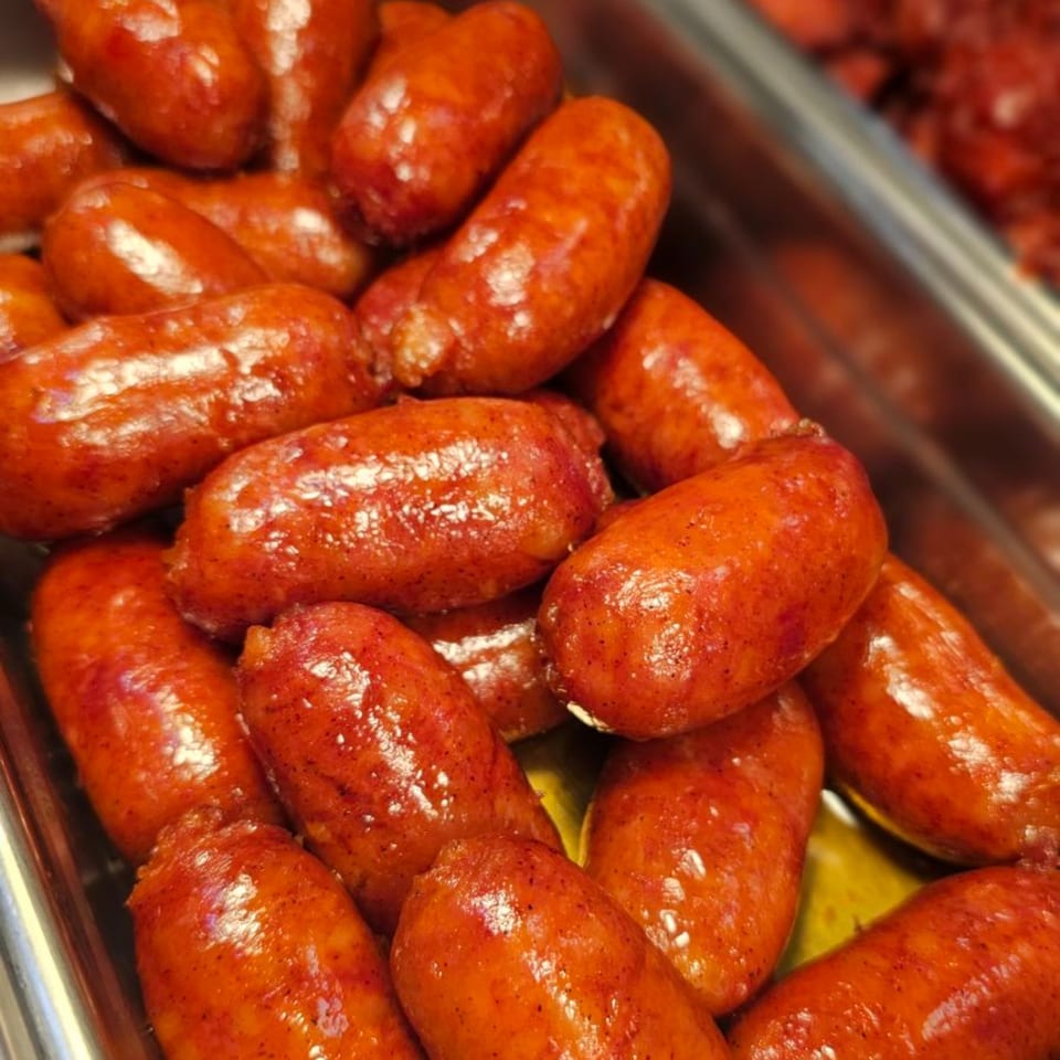 Close-up of numerous glistening, reddish-brown Filipino longganisa sausages in a metal tray.