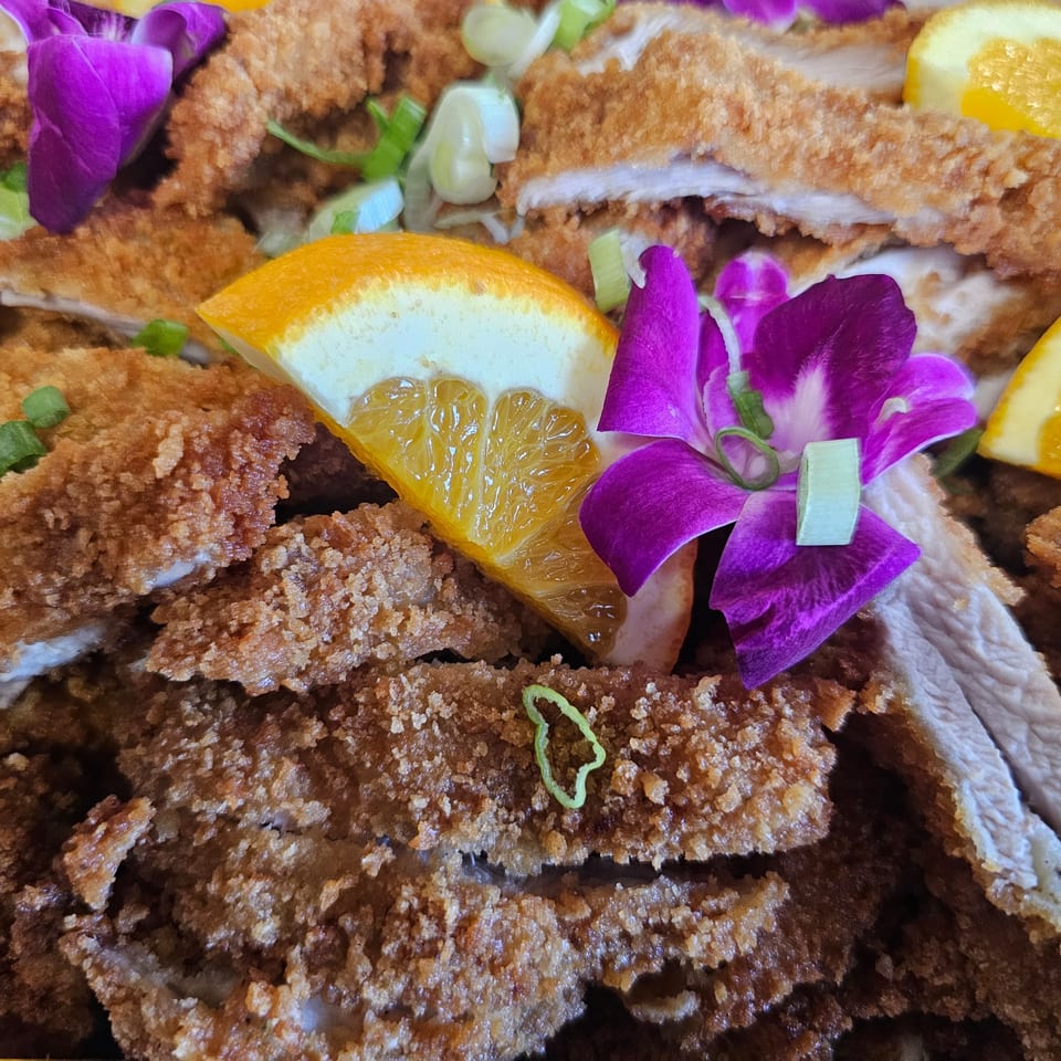 Crispy fried chicken cutlets garnished with orange slices, green onions, and purple orchids.
