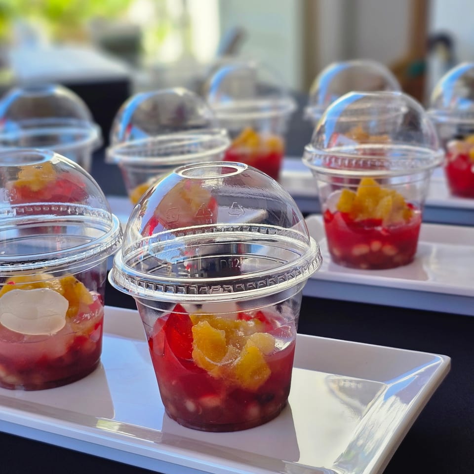 Rows of Kujo Eats' Filipino fruit desserts in clear plastic cups with dome lids on white trays.
