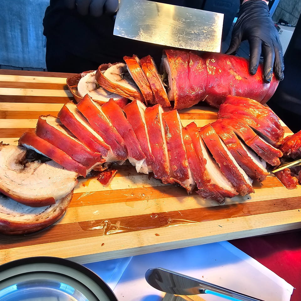 A chef in black gloves carves a large, crispy-skinned Filipino lechon belly on a wooden board.
