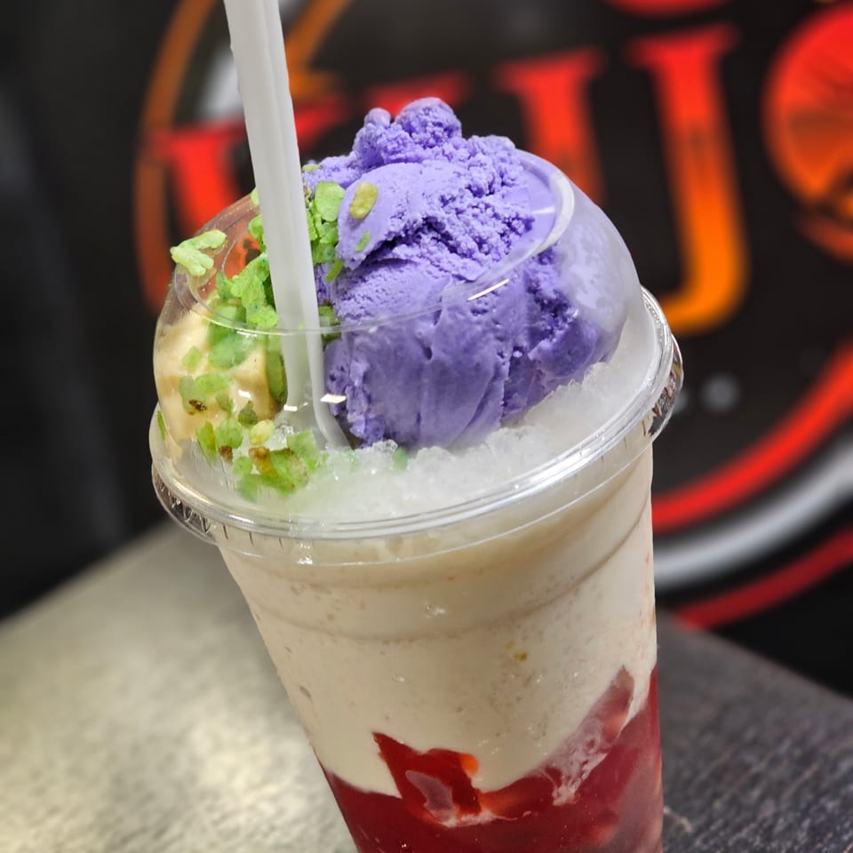 Halo-halo dessert with purple ube ice cream, green toppings, and red syrup in a clear cup.