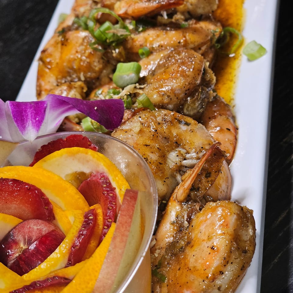 Filipino garlic butter shrimp with green onions on a white plate, next to a fruit cup.