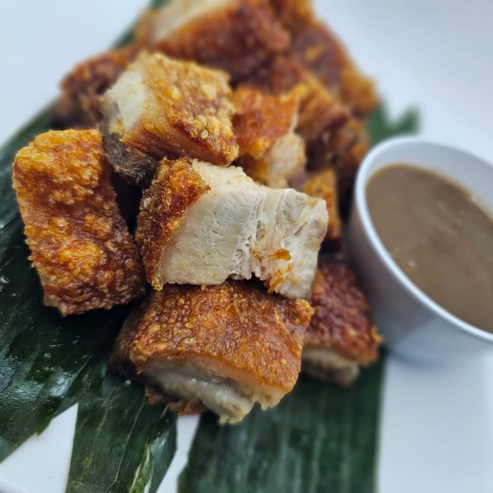 Crispy Filipino lechon kawali pork belly pieces on banana leaves with a side of sauce.
