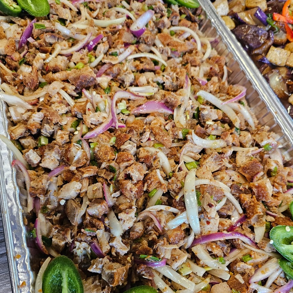 Close-up of Kujo Eats' Filipino sisig with chopped pork, onions, and green chilies in a foil tray.
