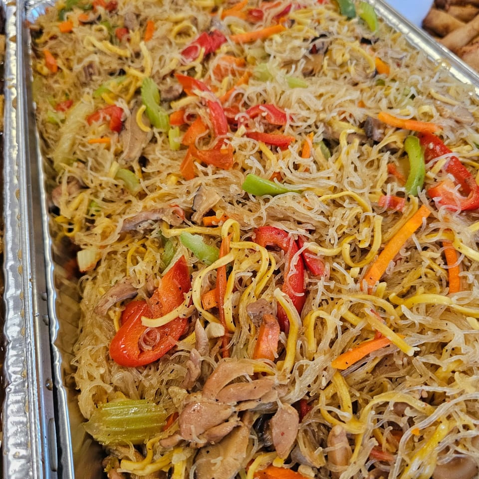 A large tray of Filipino pancit, with noodles, chicken, and colorful vegetables.