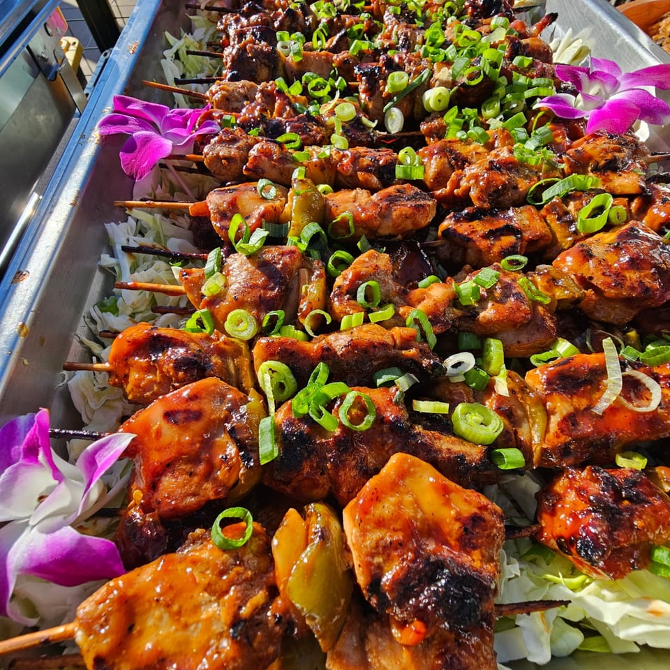 Filipino chicken skewers with green onions and purple orchids on a bed of shredded cabbage.