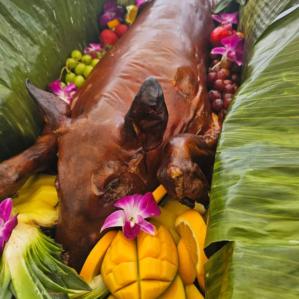 Whole roasted pig (lechon) on banana leaves, garnished with fruit and orchids.