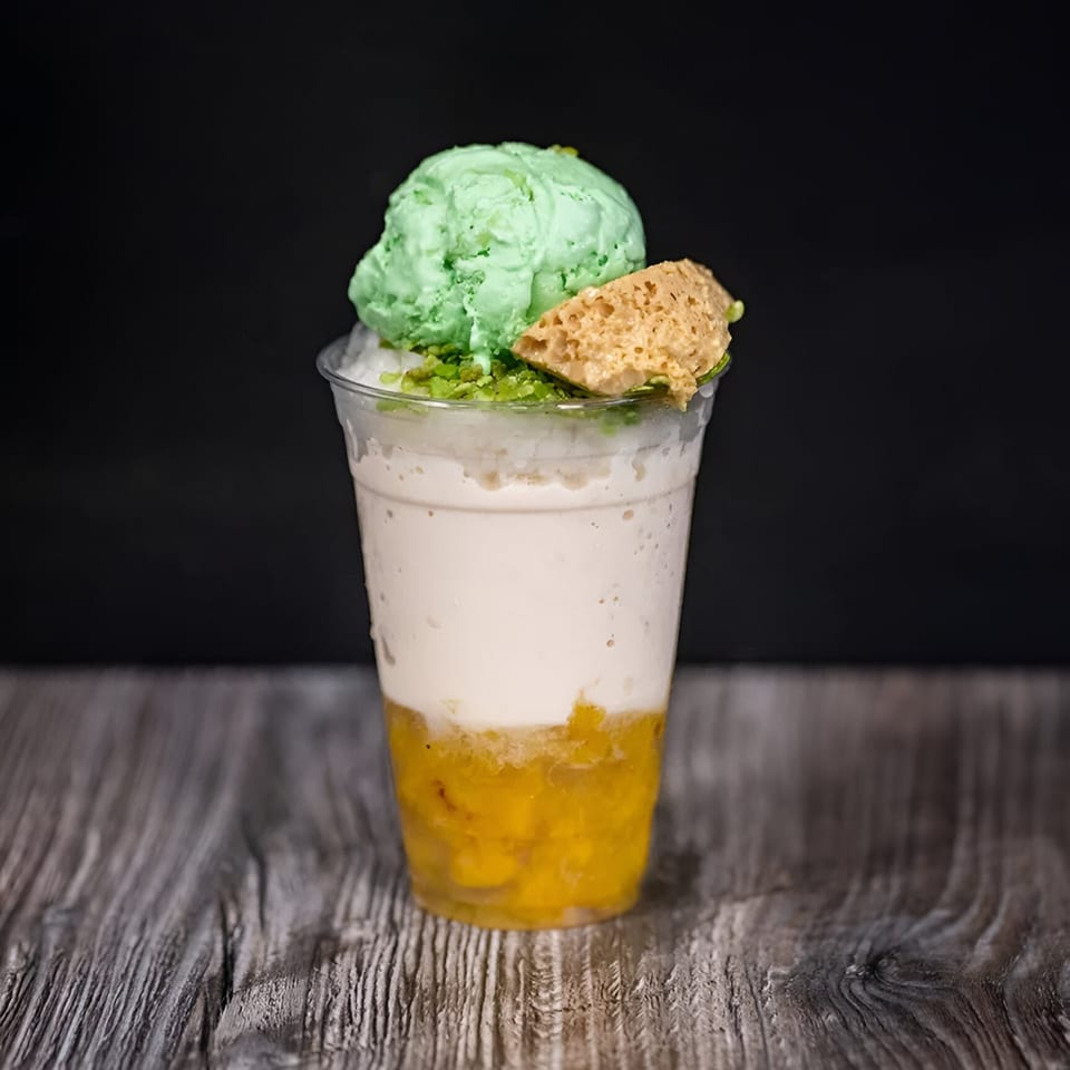 Filipino halo-halo dessert with green ice cream, crushed ice, and fruit in a clear cup.